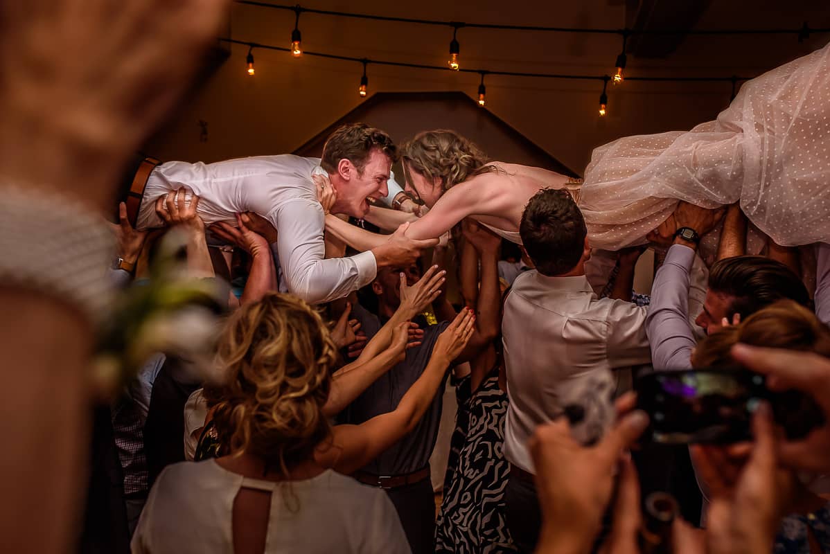 bride and groom being lifted up by people at a wedding